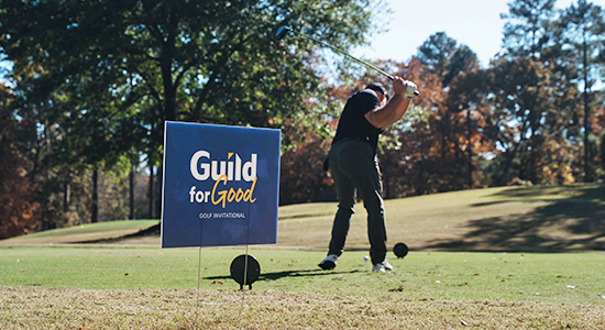 Golfer hitting in front of Guild for Good sign