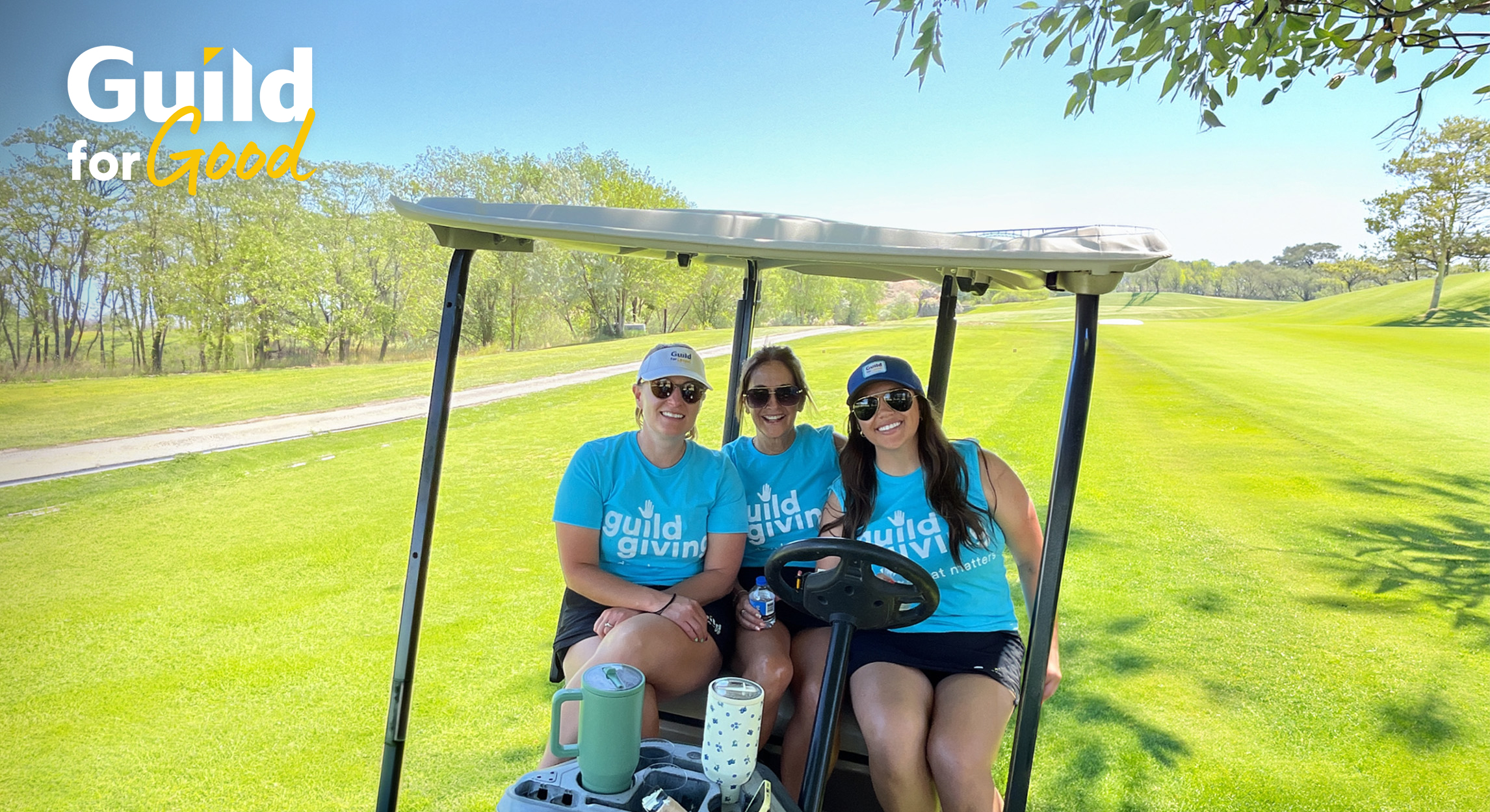 Guild Giving volunteers smile from a golf cart on a golf course at a fundraising golf event
